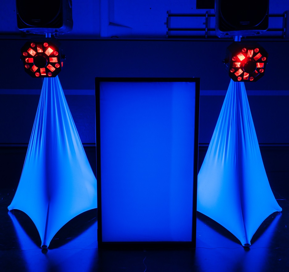 A vibrant mobile DJ setup is shown with a central blue-illuminated screen, flanked by two tall speaker stands draped in blue fabric. Each stand features a red light fixture emitting beams in various directions, creating a dynamic and electrifying party atmosphere.
